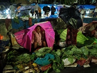 A woman covers her stall with a plastic sheet and waits for customers during rainfall in Kolkata, India, on September 25, 2024. (