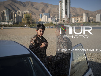 Two Iranian schoolboys wear Islamic Revolutionary Guard Corps (IRGC) military uniforms while preparing to take part in a war game, which is...