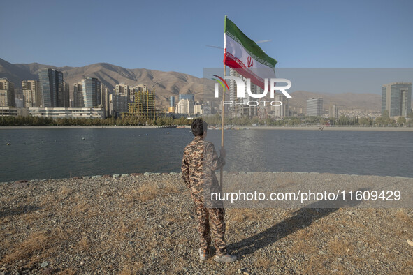 An Iranian schoolboy wearing an Islamic Revolutionary Guard Corps (IRGC) military uniform holds an Iranian flag while taking part in a war g...