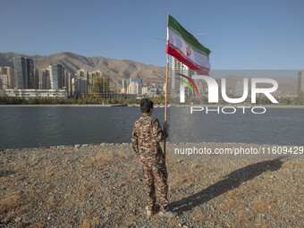 An Iranian schoolboy wearing an Islamic Revolutionary Guard Corps (IRGC) military uniform holds an Iranian flag while taking part in a war g...