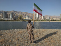 An Iranian schoolboy wearing an Islamic Revolutionary Guard Corps (IRGC) military uniform holds an Iranian flag while taking part in a war g...