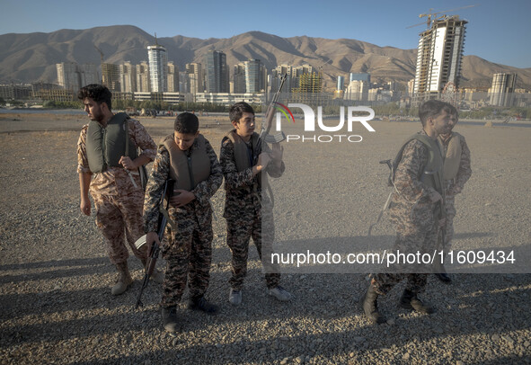 Two Iranian schoolboys wear Islamic Revolutionary Guard Corps (IRGC) military uniforms and hold AK-45 rifles while preparing to take part in...