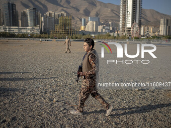 An Iranian schoolboy wears an Islamic Revolutionary Guard Corps (IRGC) military uniform and carries an AK-45 rifle while preparing to take p...