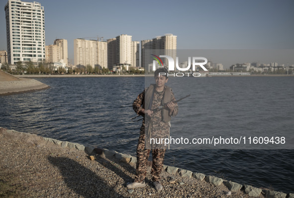 An Iranian schoolboy wearing an Islamic Revolutionary Guard Corps (IRGC) military uniform poses for a photograph as he holds an AK-45 rifle,...