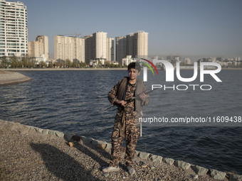 An Iranian schoolboy wearing an Islamic Revolutionary Guard Corps (IRGC) military uniform poses for a photograph as he holds an AK-45 rifle,...