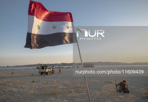 A member of the Islamic Revolutionary Guard Corps (IRGC) sits next to an Iraqi flag while taking part in a war game, which is a reconstructi...