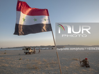 A member of the Islamic Revolutionary Guard Corps (IRGC) sits next to an Iraqi flag while taking part in a war game, which is a reconstructi...