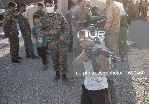 An Iranian schoolboy holds an AK-45 rifle while Islamic Revolutionary Guard Corps (IRGC) military personnel prepare to take part in a war ga...