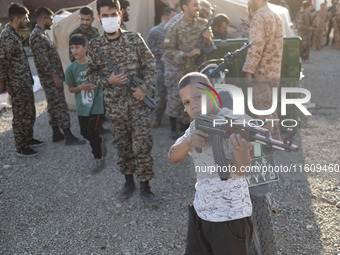 An Iranian schoolboy holds an AK-45 rifle while Islamic Revolutionary Guard Corps (IRGC) military personnel prepare to take part in a war ga...