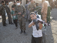 An Iranian schoolboy holds an AK-45 rifle while Islamic Revolutionary Guard Corps (IRGC) military personnel prepare to take part in a war ga...