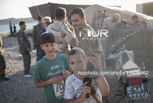 An Iranian schoolboy holds an AK-45 rifle while Islamic Revolutionary Guard Corps (IRGC) military personnel prepare to take part in a war ga...