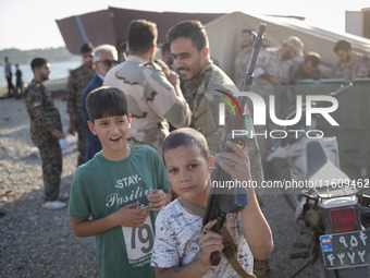 An Iranian schoolboy holds an AK-45 rifle while Islamic Revolutionary Guard Corps (IRGC) military personnel prepare to take part in a war ga...