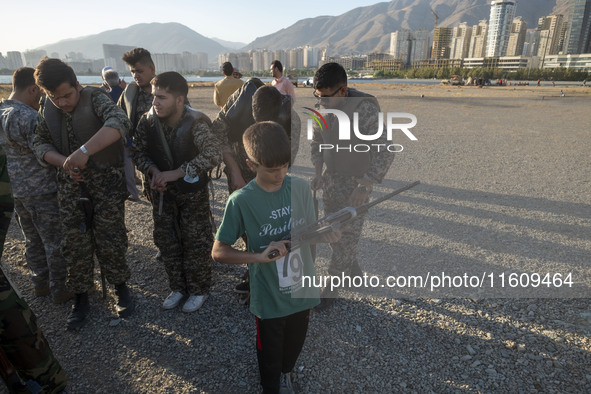 An Iranian schoolboy holds an AK-45 rifle while Islamic Revolutionary Guard Corps (IRGC) military personnel prepare to take part in a war ga...