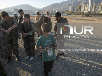 An Iranian schoolboy holds an AK-45 rifle while Islamic Revolutionary Guard Corps (IRGC) military personnel prepare to take part in a war ga...