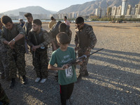 An Iranian schoolboy holds an AK-45 rifle while Islamic Revolutionary Guard Corps (IRGC) military personnel prepare to take part in a war ga...