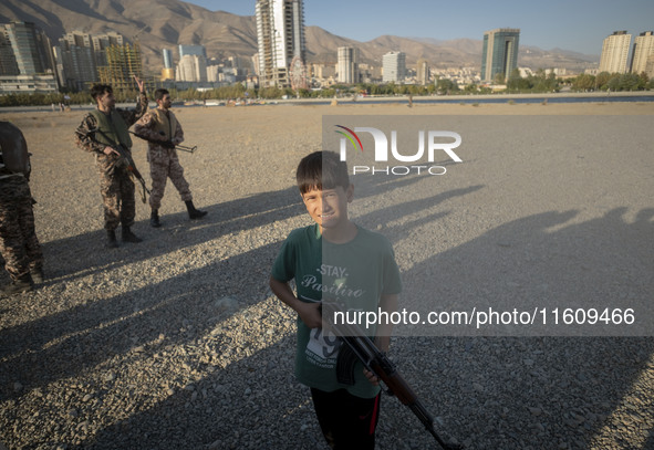 An Iranian schoolboy holds an AK-45 rifle while Islamic Revolutionary Guard Corps (IRGC) military personnel prepare to take part in a war ga...