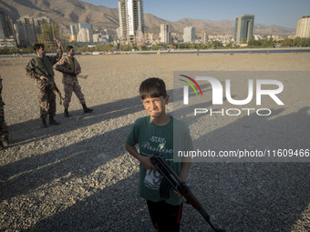 An Iranian schoolboy holds an AK-45 rifle while Islamic Revolutionary Guard Corps (IRGC) military personnel prepare to take part in a war ga...