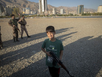 An Iranian schoolboy holds an AK-45 rifle while Islamic Revolutionary Guard Corps (IRGC) military personnel prepare to take part in a war ga...