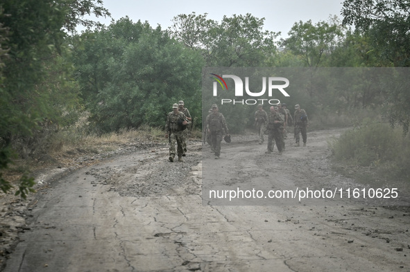 Servicemen of the 65th Separate Mechanized Brigade of the Armed Forces of Ukraine march along a dusty road during combat coordination in Ukr...