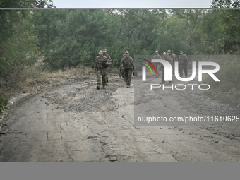 Servicemen of the 65th Separate Mechanized Brigade of the Armed Forces of Ukraine march along a dusty road during combat coordination in Ukr...