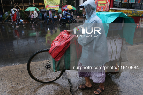 A street food vendor covered with a plastic sheet with his cycle-loaded goods crosses a busy street as it rains in Kolkata, India, on Septem...