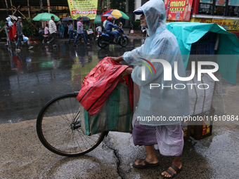 A street food vendor covered with a plastic sheet with his cycle-loaded goods crosses a busy street as it rains in Kolkata, India, on Septem...