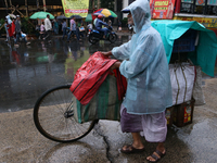 A street food vendor covered with a plastic sheet with his cycle-loaded goods crosses a busy street as it rains in Kolkata, India, on Septem...