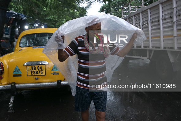 A laborer covers themselves with plastic sheets to protect from the monsoon rain in Kolkata, India, on September 26, 2024. 