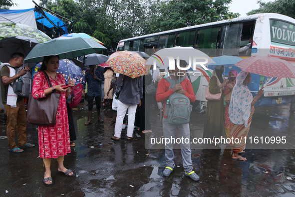 People hold umbrellas and wait for transportation in the monsoon rain in Kolkata, India, on September 26, 2024. 