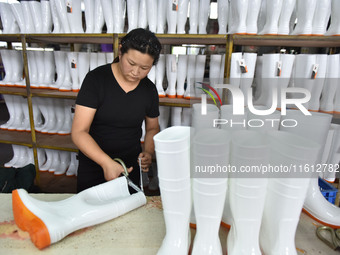 A worker works on a production line of rain rubber shoes at Guanhong Plastic Industry Co., LTD in Jieshou, China, on September 27, 2024. (