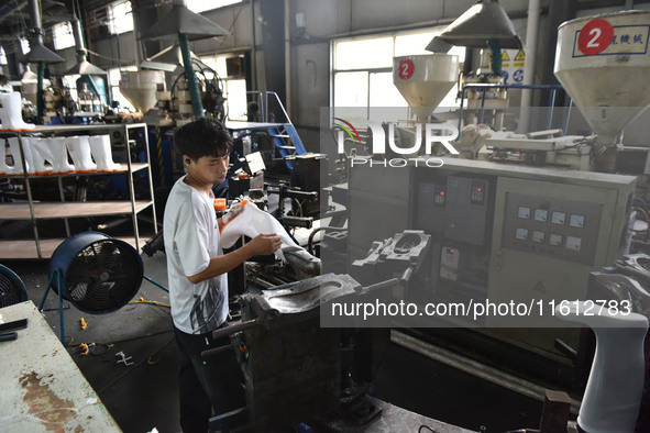 A worker works on a production line of rain rubber shoes at Guanhong Plastic Industry Co., LTD in Jieshou, China, on September 27, 2024. 