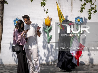 Two young veiled women carry an Iranian flag and a flag of Lebanon's Hezbollah as they walk past two young people, one of whom is not wearin...