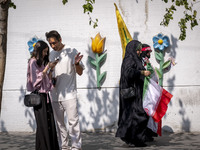 Two young veiled women carry an Iranian flag and a flag of Lebanon's Hezbollah as they walk past two young people, one of whom is not wearin...