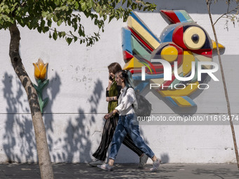 Two young Iranian women who do not wear mandatory headscarves walk along a sidewalk during Friday prayers ceremonies, before an anti-Israeli...