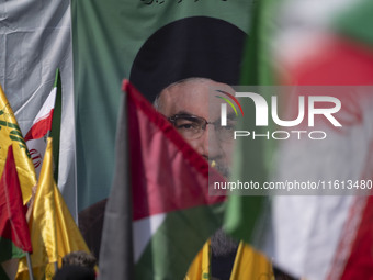 Iranian worshippers wave a Palestinian flag and an Iranian flag in front of a portrait of Lebanon's Hezbollah Secretary General, Hassan Nasr...