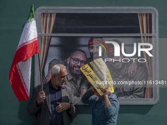 Two Iranian worshippers talk to each other as they hold an Israeli placard and an Iranian flag while standing in front of symbolic portraits...