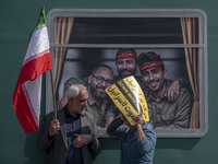 Two Iranian worshippers talk to each other as they hold an Israeli placard and an Iranian flag while standing in front of symbolic portraits...