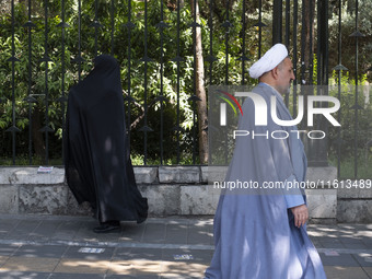 A veiled Iranian worshipper and a cleric walk along a sidewalk to the University of Tehran to take part in a Friday prayers ceremony before...