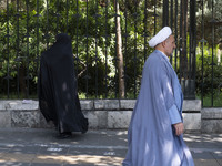 A veiled Iranian worshipper and a cleric walk along a sidewalk to the University of Tehran to take part in a Friday prayers ceremony before...