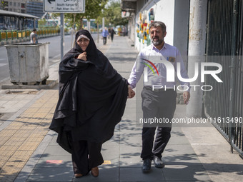 An Iranian couple walks along a sidewalk to the University of Tehran to take part in a Friday prayers ceremony before an anti-Israeli protes...