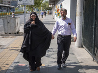 An Iranian couple walks along a sidewalk to the University of Tehran to take part in a Friday prayers ceremony before an anti-Israeli protes...