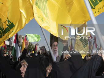 Iranian worshippers wave Lebanon's Hezbollah flags as one of them holds a portrait of Iran's Supreme Leader, Ayatollah Ali Khamenei, while t...