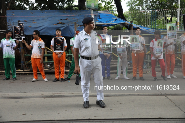 A police officer stands guard while school students make a human chain and hold posters during a Global Climate Strike march in Kolkata, Ind...