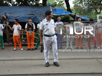 A police officer stands guard while school students make a human chain and hold posters during a Global Climate Strike march in Kolkata, Ind...