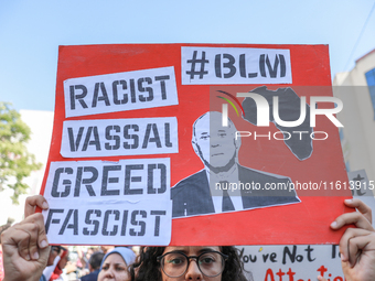 A female demonstrator raises a placard with a caricature of Tunisian President Kais Saied that reads, ''racist, vassal, greed, fascist,'' du...