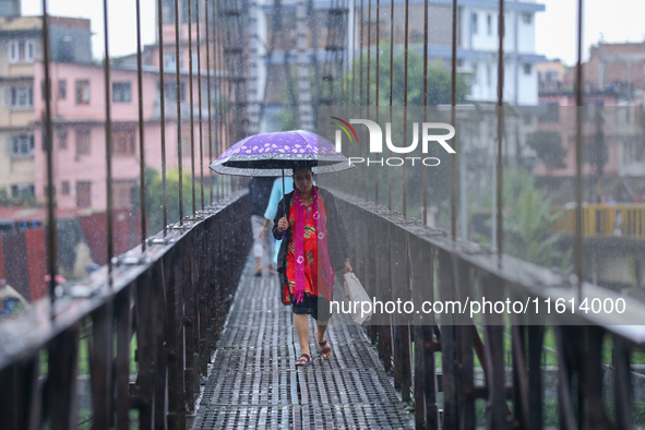 A Nepali woman wearing an umbrella crosses a suspension bridge following incessant rainfall after the red alert issued by Nepal's weather de...