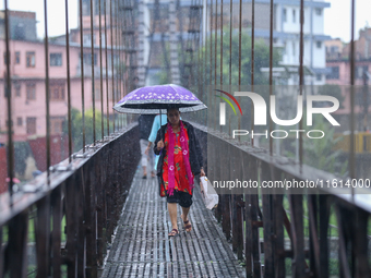 A Nepali woman wearing an umbrella crosses a suspension bridge following incessant rainfall after the red alert issued by Nepal's weather de...