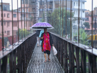 A Nepali woman wearing an umbrella crosses a suspension bridge following incessant rainfall after the red alert issued by Nepal's weather de...