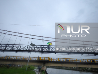 A Nepali man wearing an umbrella crosses a suspension bridge following incessant rainfall after the red alert issued by Nepal's weather depa...