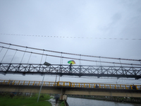 A Nepali man wearing an umbrella crosses a suspension bridge following incessant rainfall after the red alert issued by Nepal's weather depa...